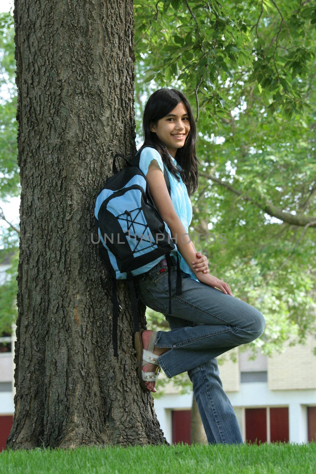 Young teen girl standing with backpack by tree, smiling. Part asian, Scandinavian descent.