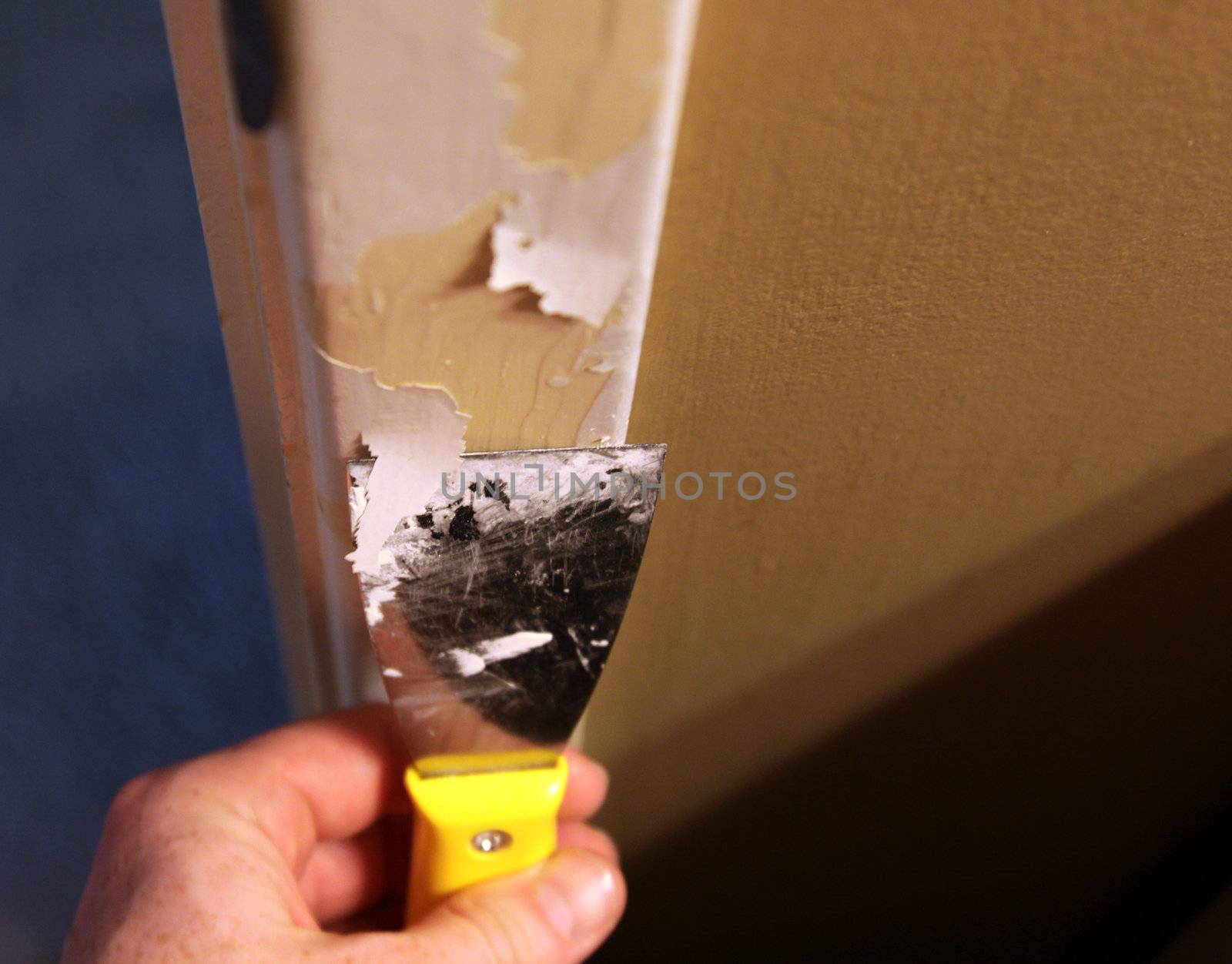 A close-up of a person stripping paint using a putty knife.
