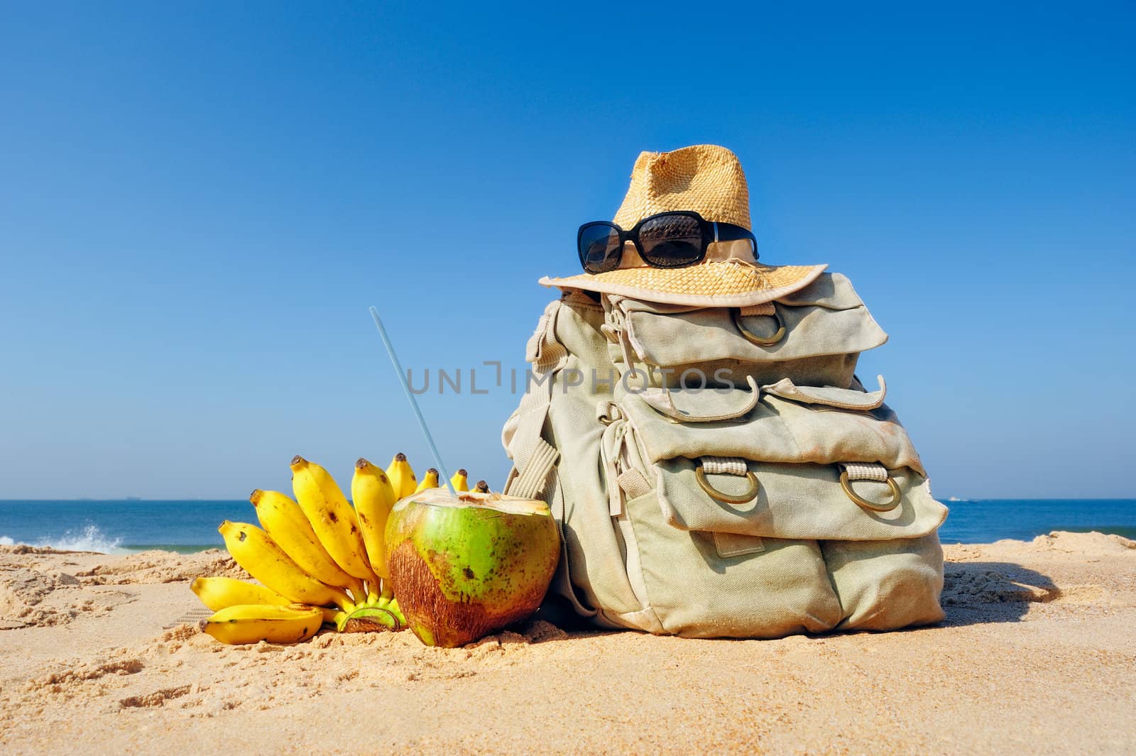 Knapsack, hat and fruit on the sandy beach