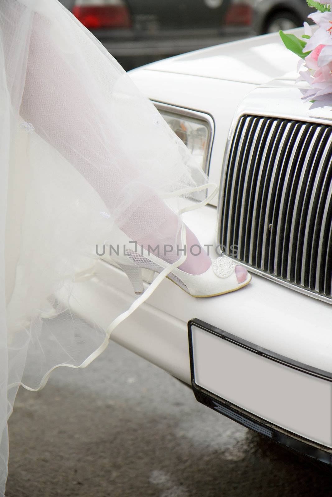 leg of the bride in white shoes on the bumper limousine