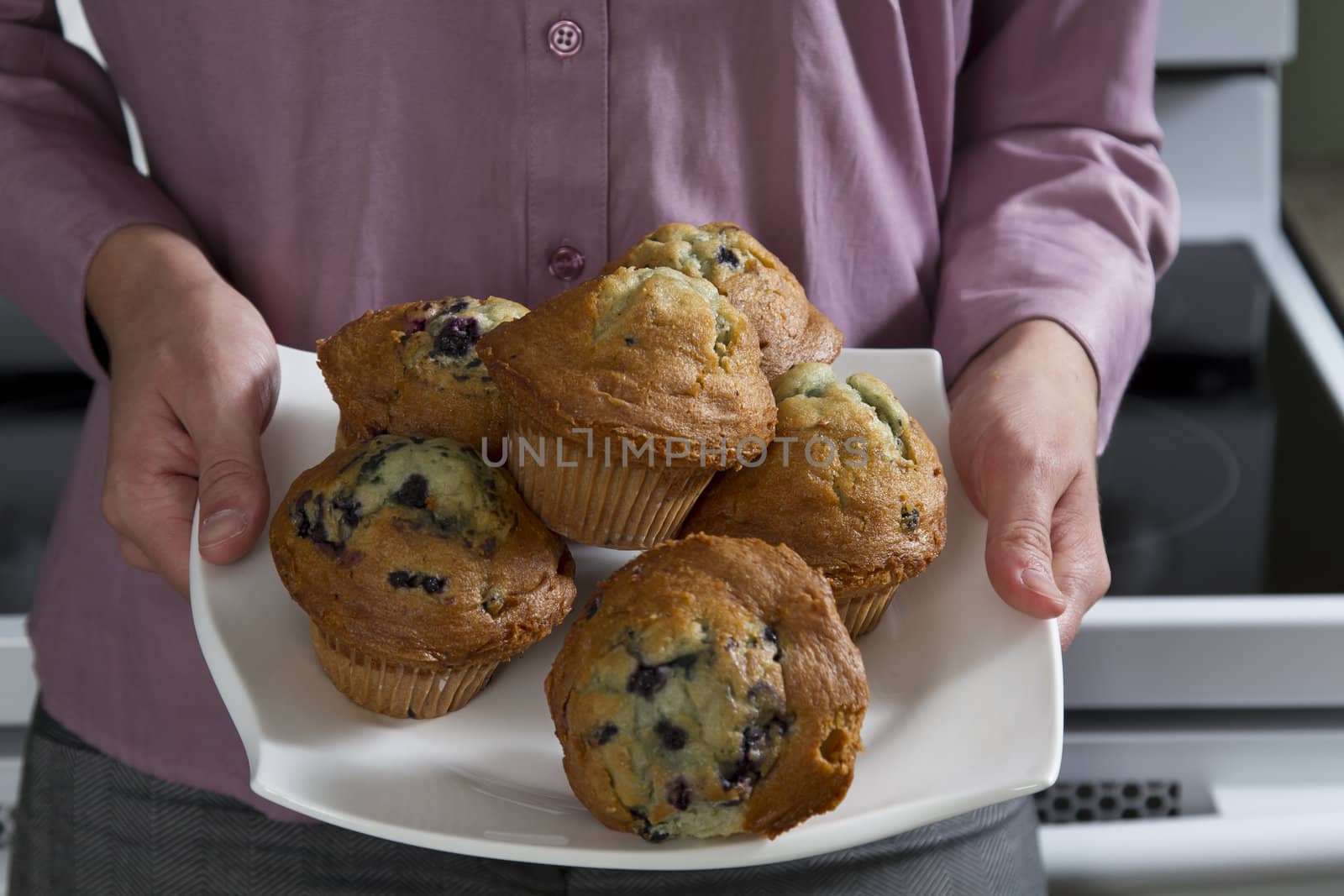 Young woman holding a plate muffins front of an oven