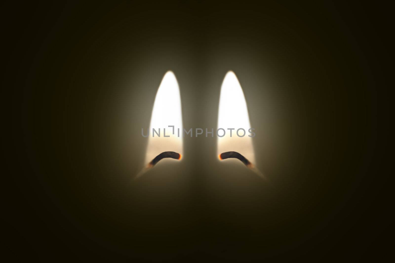 Close up on two ignited candle wicks against a black background.