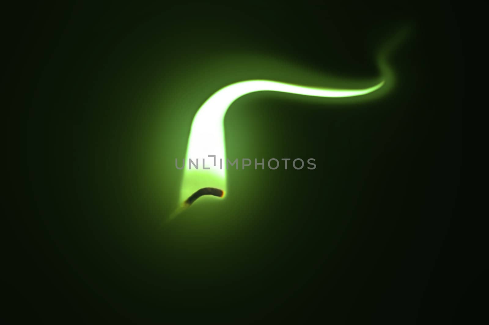 Close up on an ignited candle wick with extended green flame against a black background.