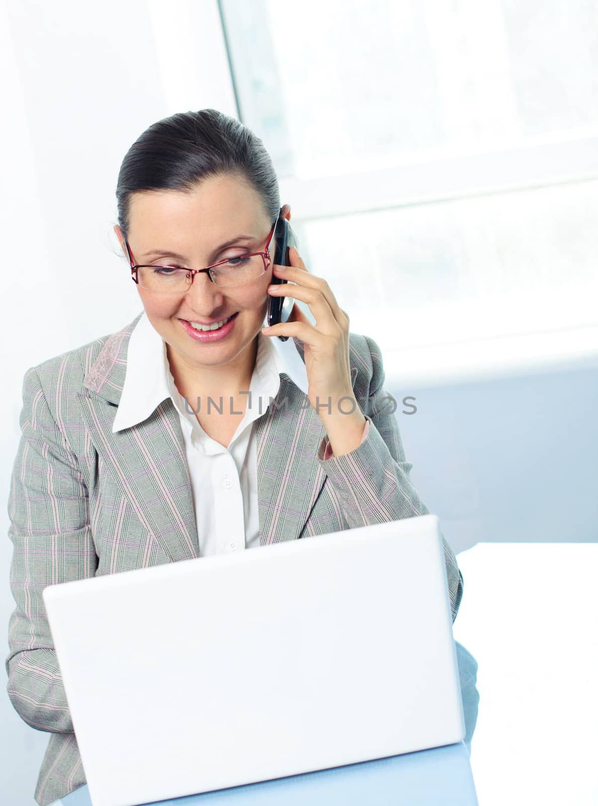 Attractive smiling young business woman with glasses using laptop at work desk