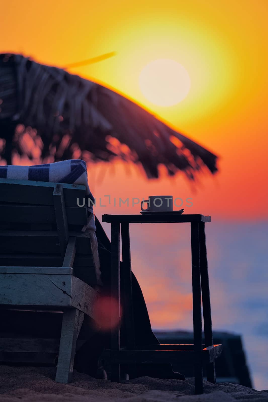 Exotic beach umbrella and deckchair on tropical coast on evening