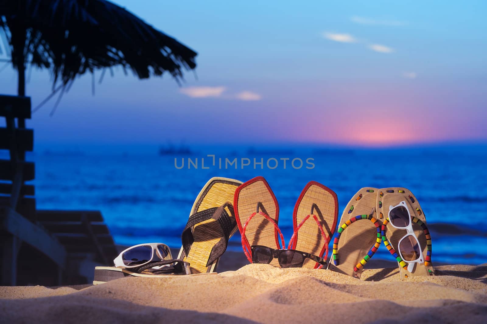 Three pair of beach sandals and glasses on the beach on evening