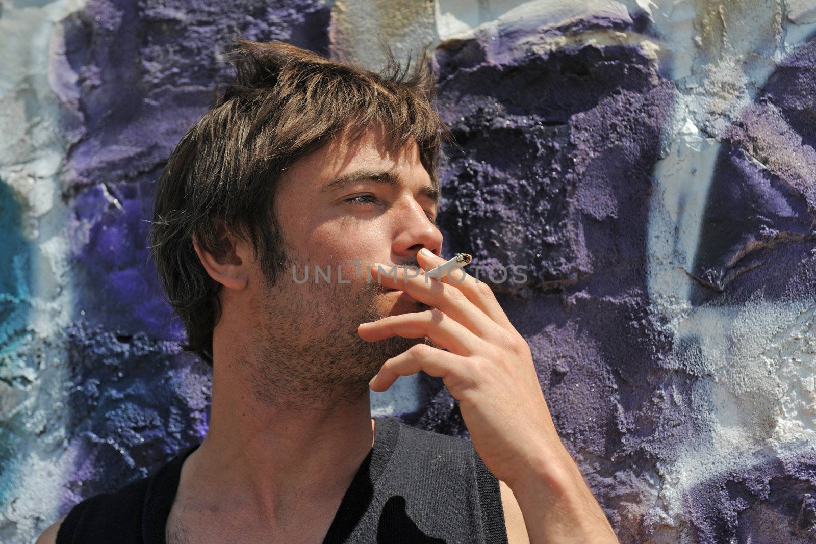 a young man smoking in front of a wall with graffitis