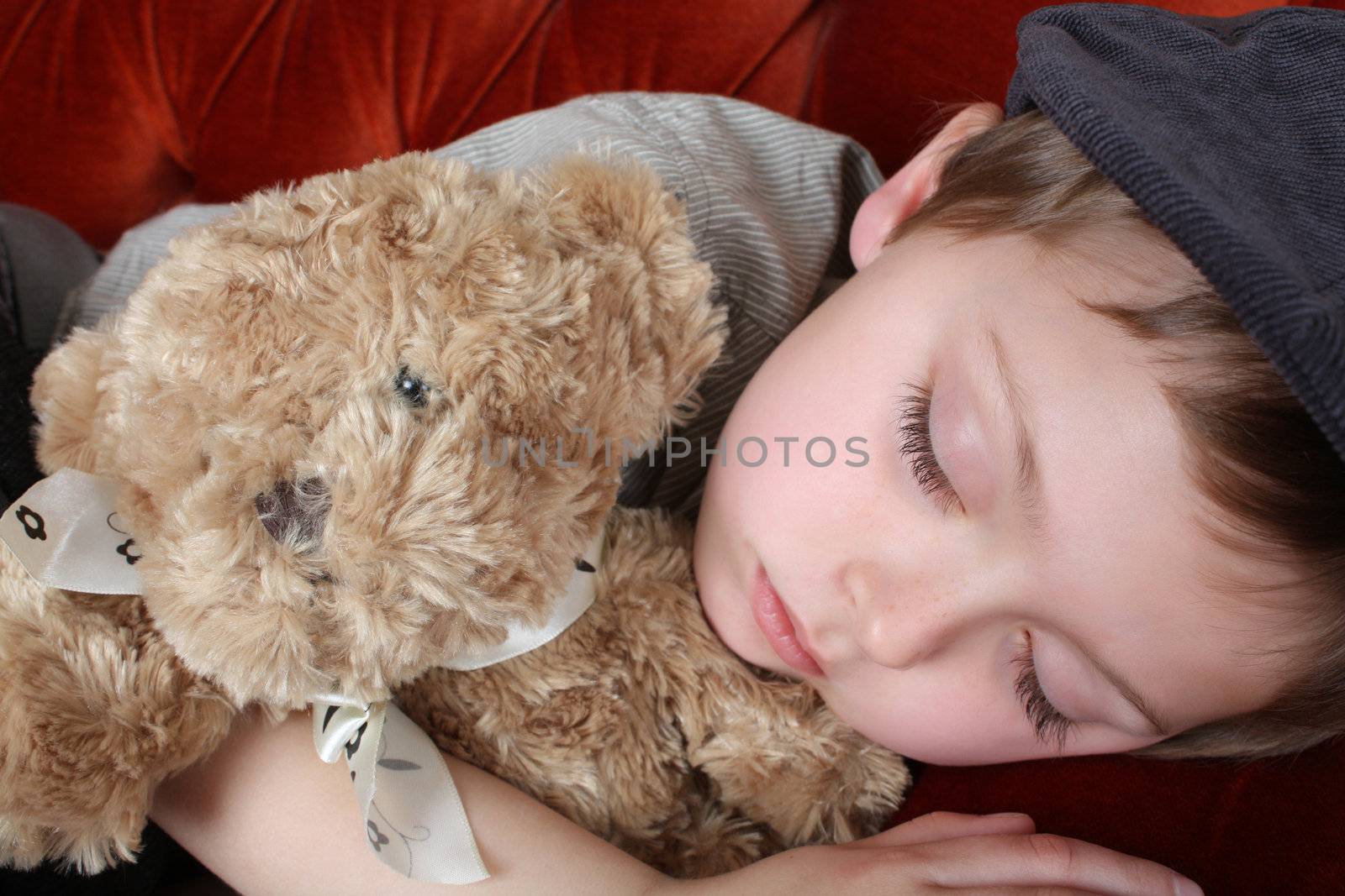 Young boy wearing a hat, sleeping holding a teddy bear