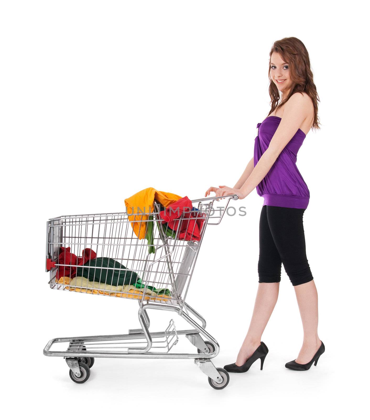 Pretty girl with shopping cart buying colorful clothing, isolated on white.