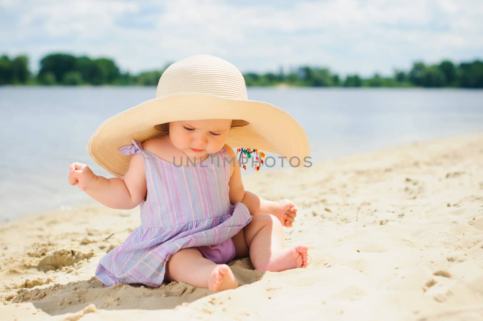 cute baby girl in a beige hat sitting and playing on the beach with sand.