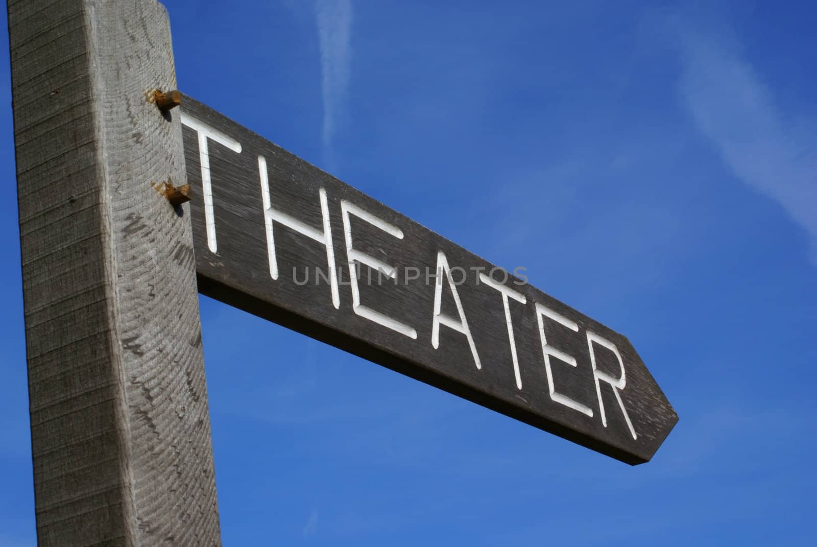 Wooden theater sign in shape of an arrow against a blue sky.           