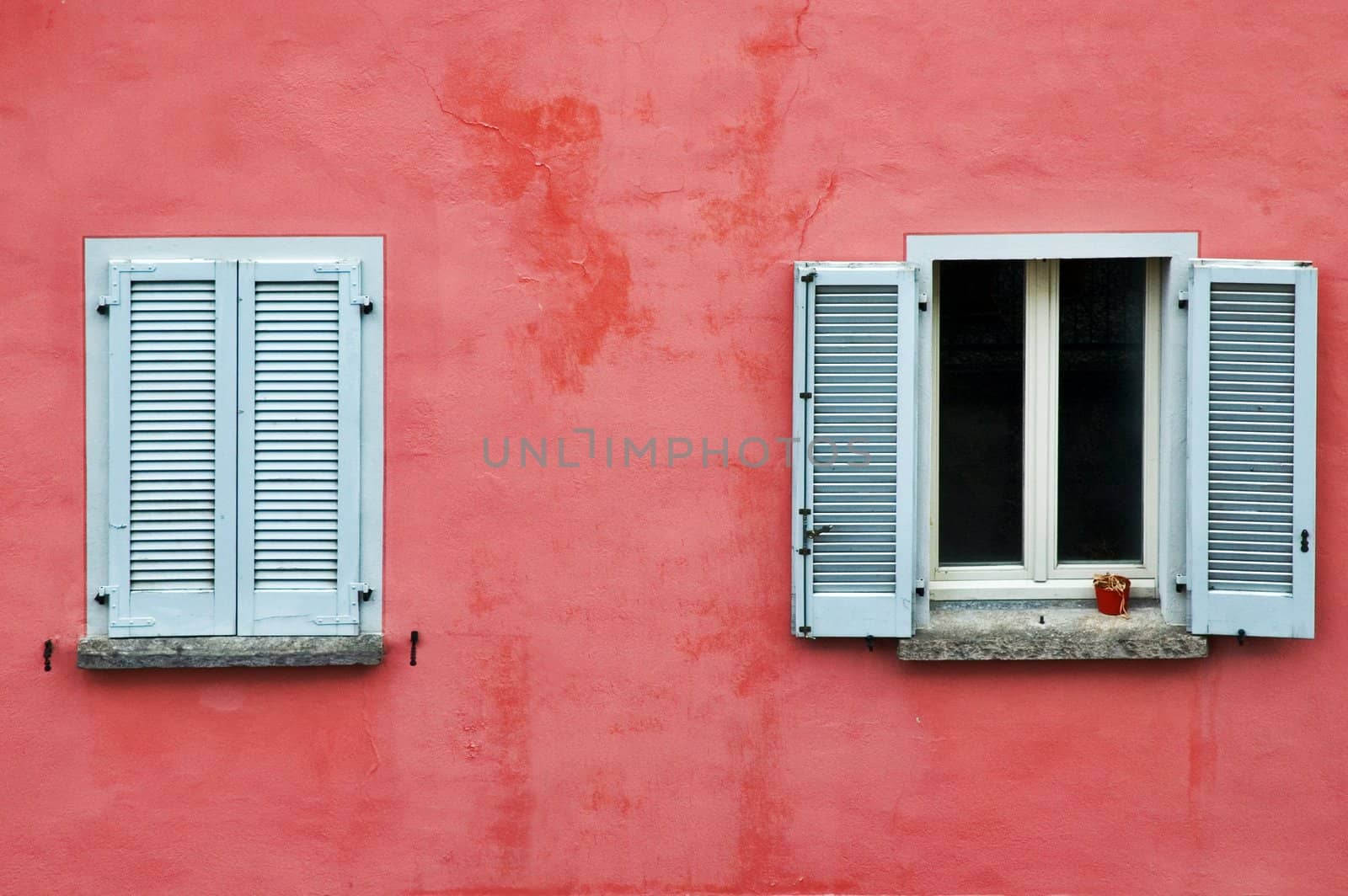 Two windows on a pink wall, one with white shutters closed