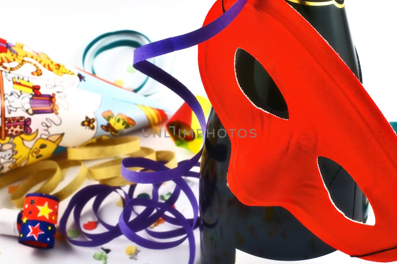 Red mask hanging from champagne bottle with confetti and streamers in the background with slight diffuse filter