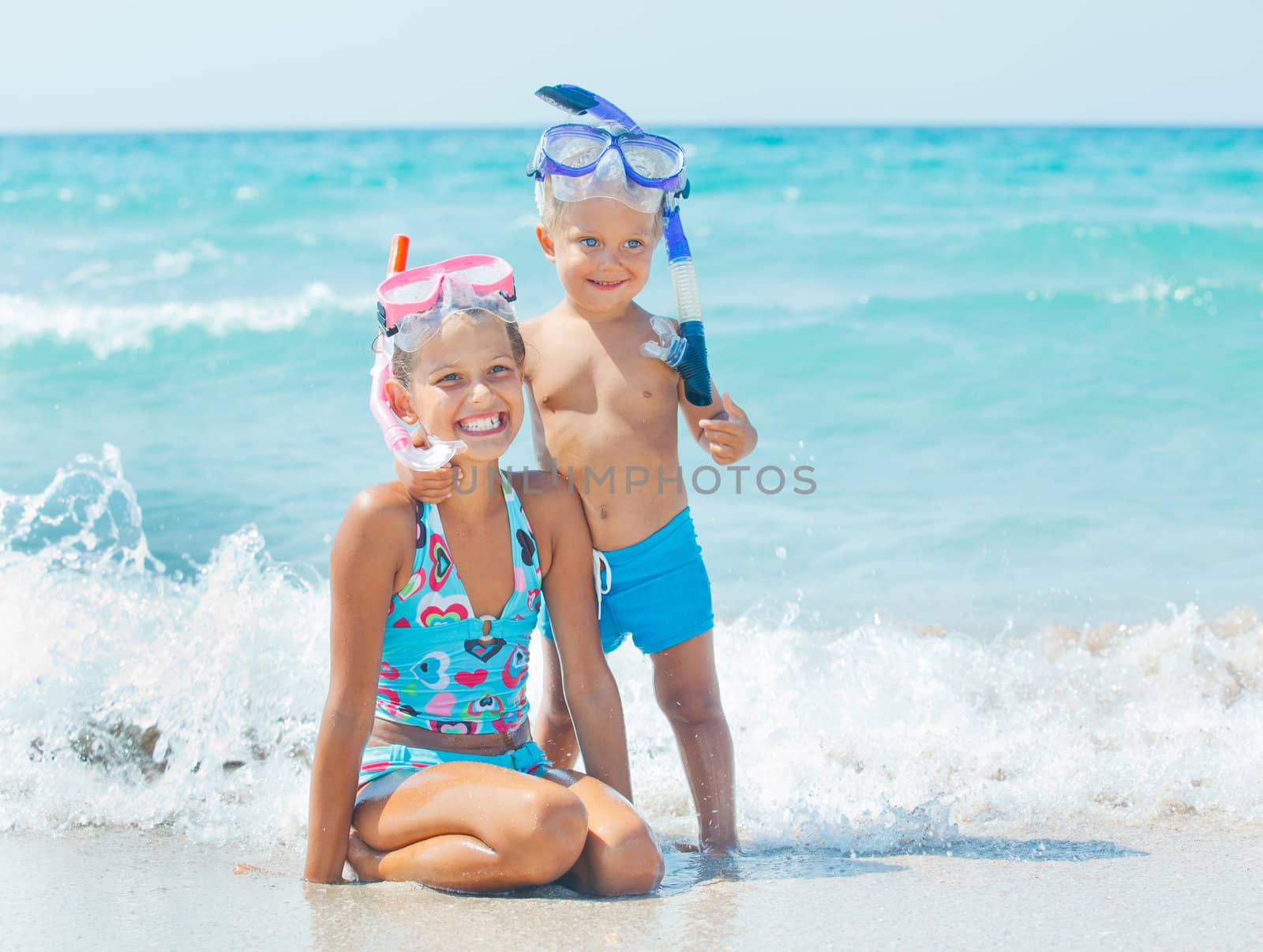 Smiling Happy brother and sister posing on a beach wearing snorkeling equipment. In the background the sea