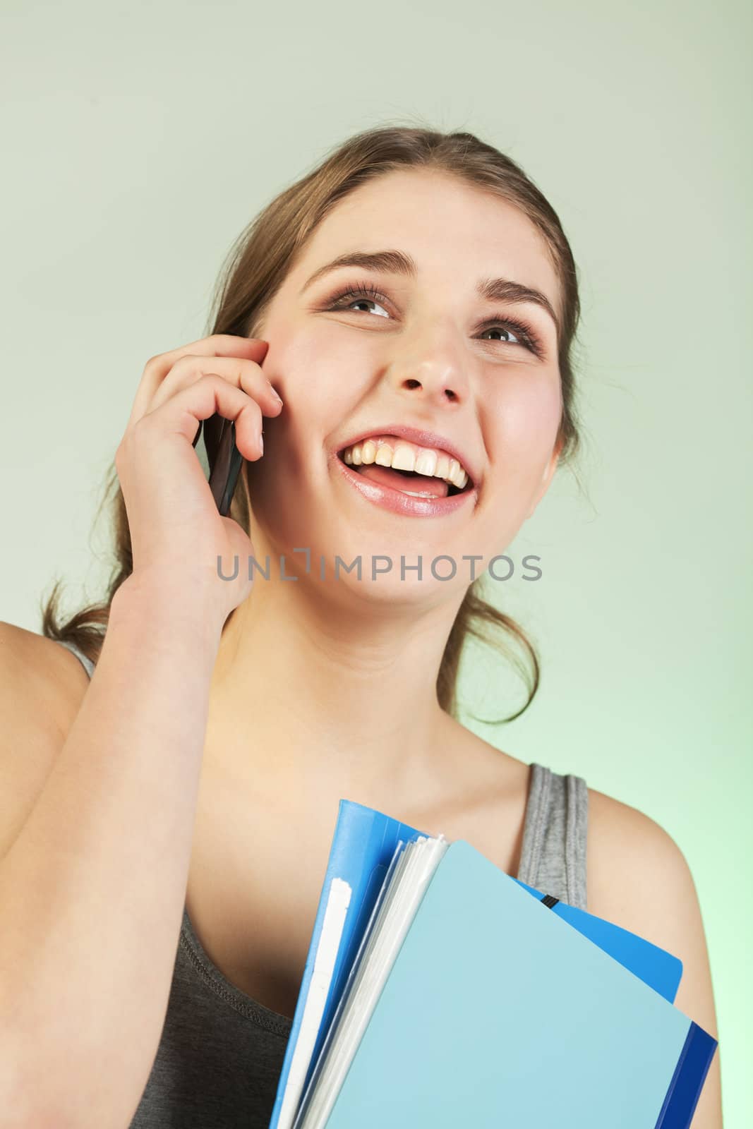 Smiling teenager girl holding blue plastic folders speaks on cellphone