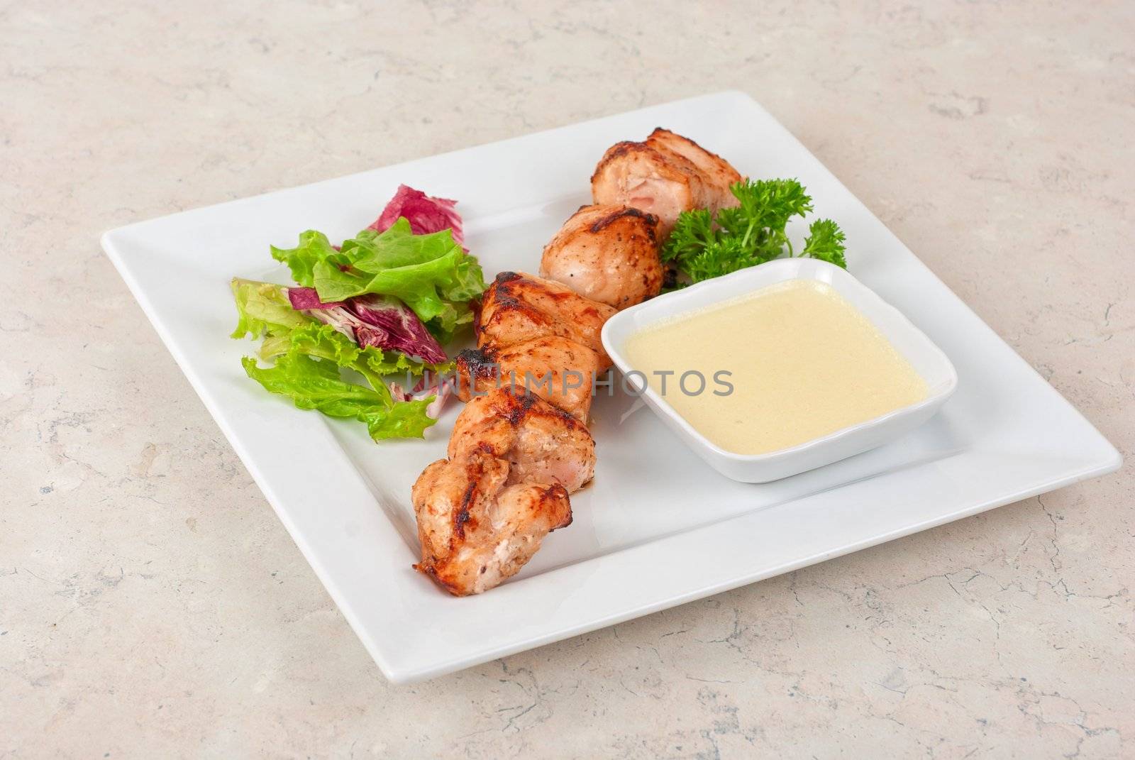 Grilled chicken kebab with sauce and greens on white plate