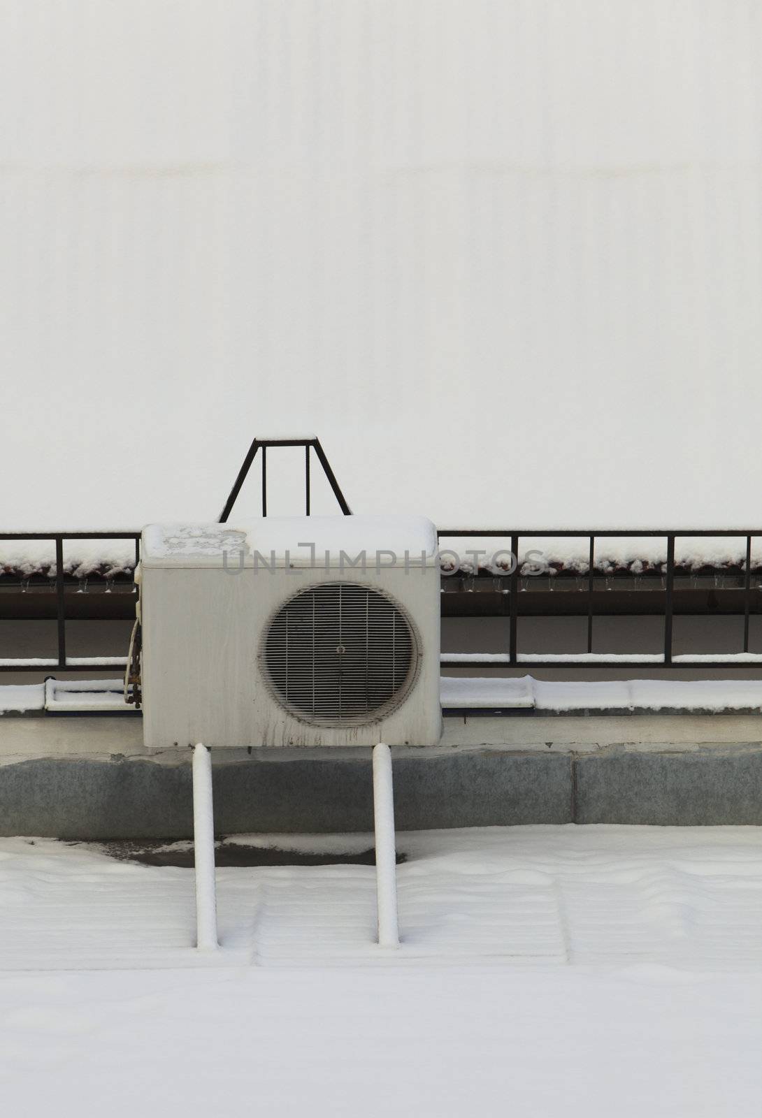 Image of an air conditioner machine on a roof of a building covered by snow.