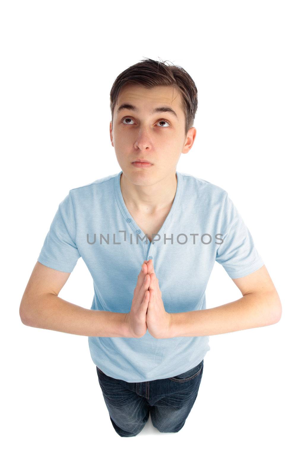 A boy kneeling with hands together in prayer.  He is looking up with hope and faith.