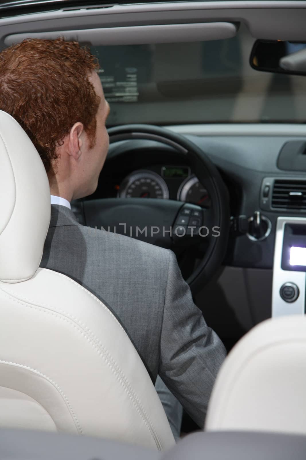 A young man in a grey suit driving a luxury convertible car