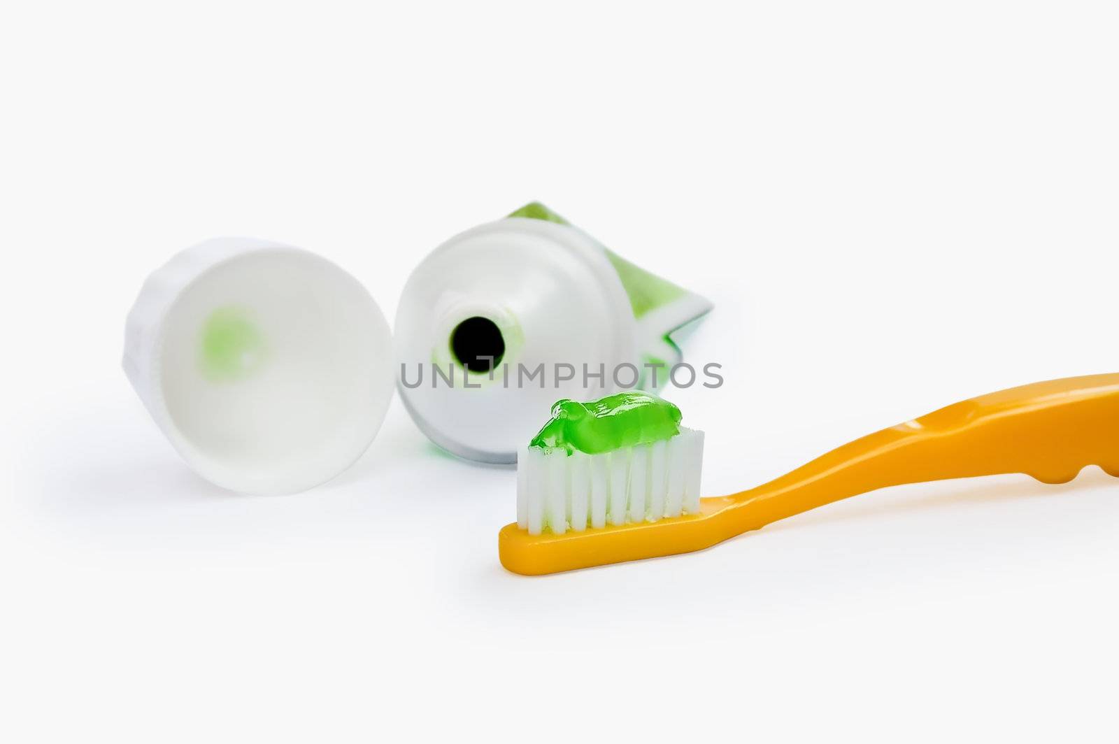Yellow toothbrush with a green transparent toothpaste tubes open cover isolated on white background