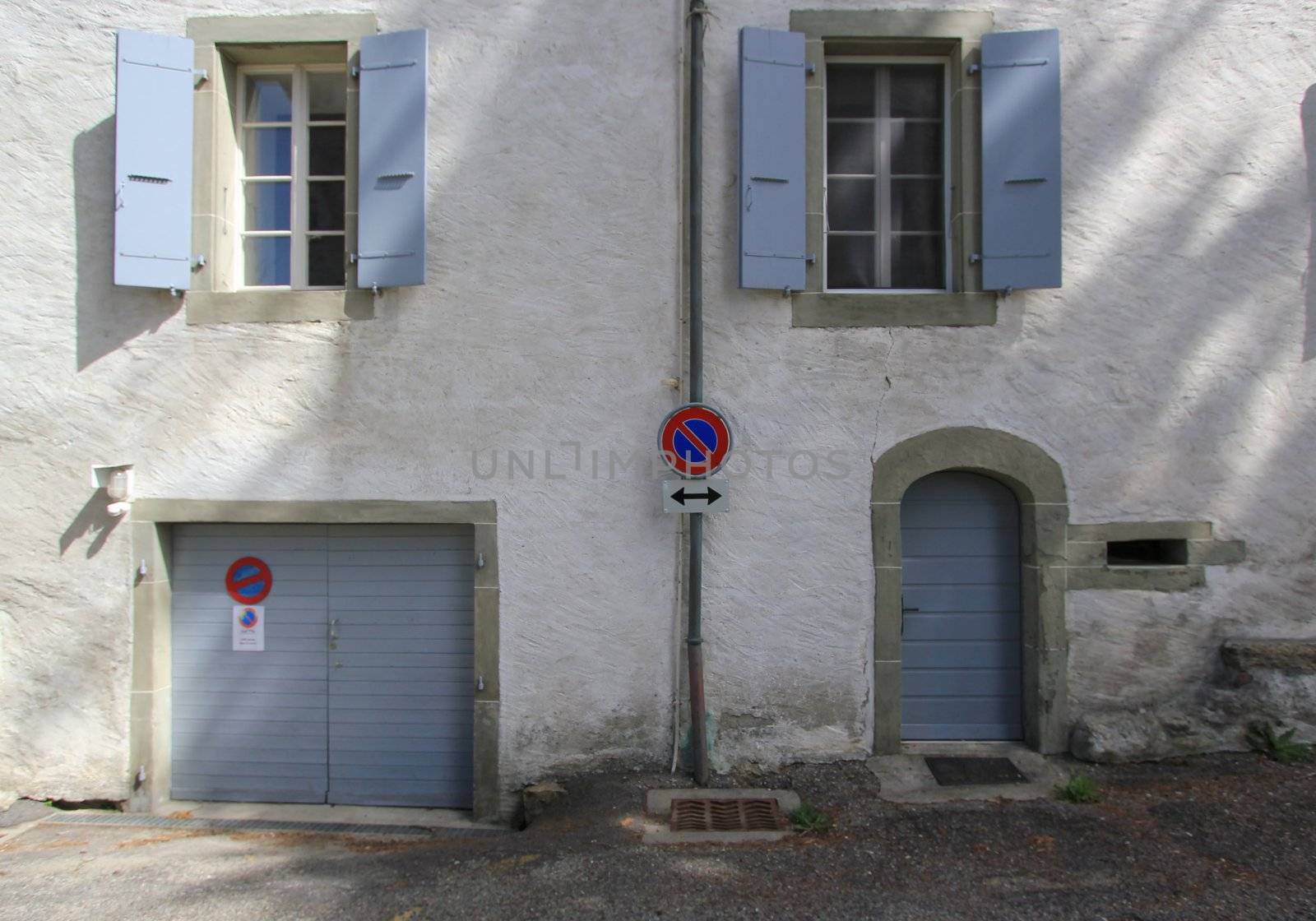 Close up of a white facade with windows, door and parking entrance and sign indicating forbidden parking