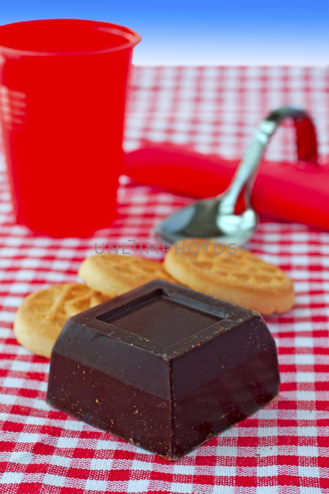 Block of chocolate over white and red cloth, with cup and biscuits in the background