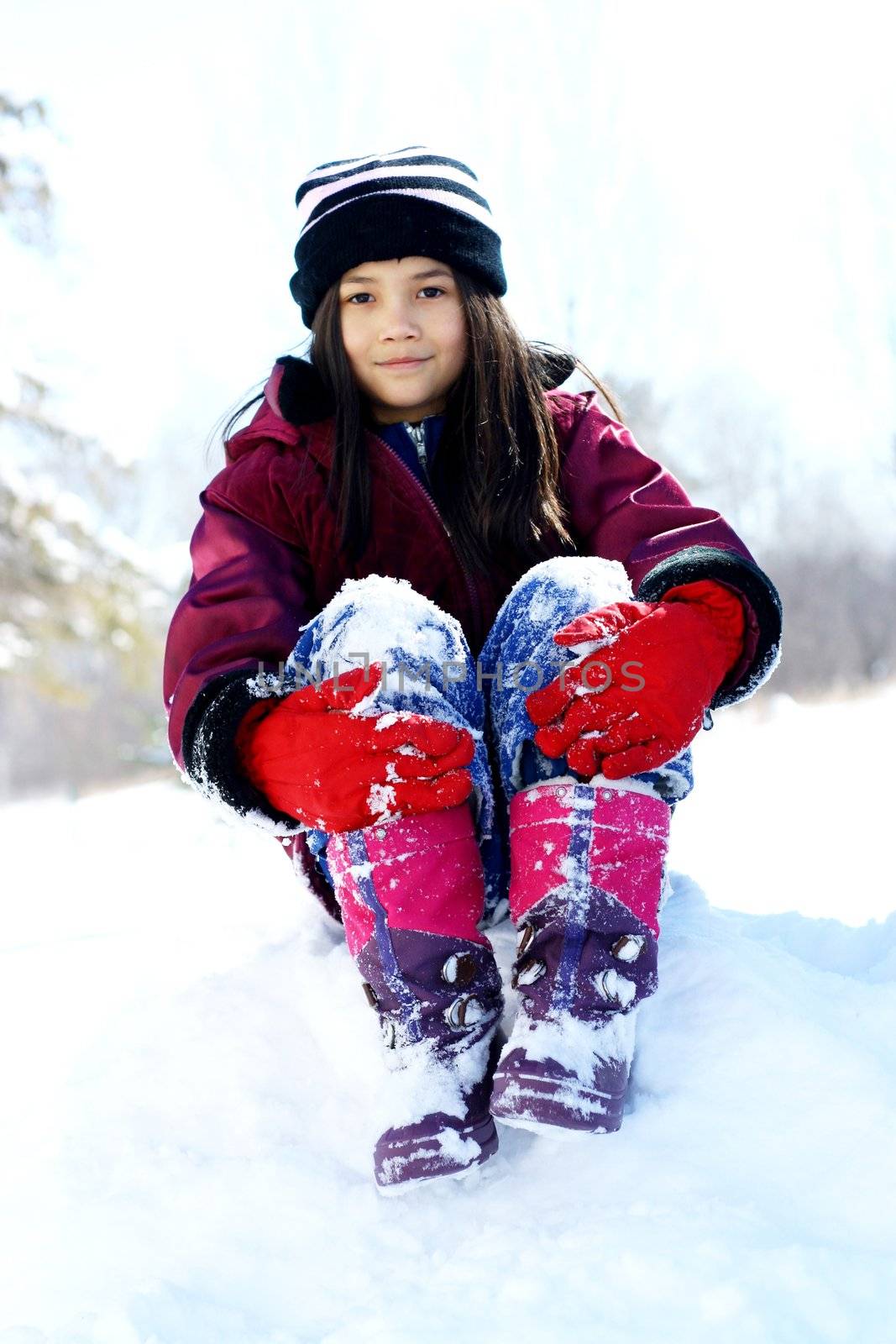Young girl in winter attire playing on top of snow hill. Part Scandinavian, part asian descent.