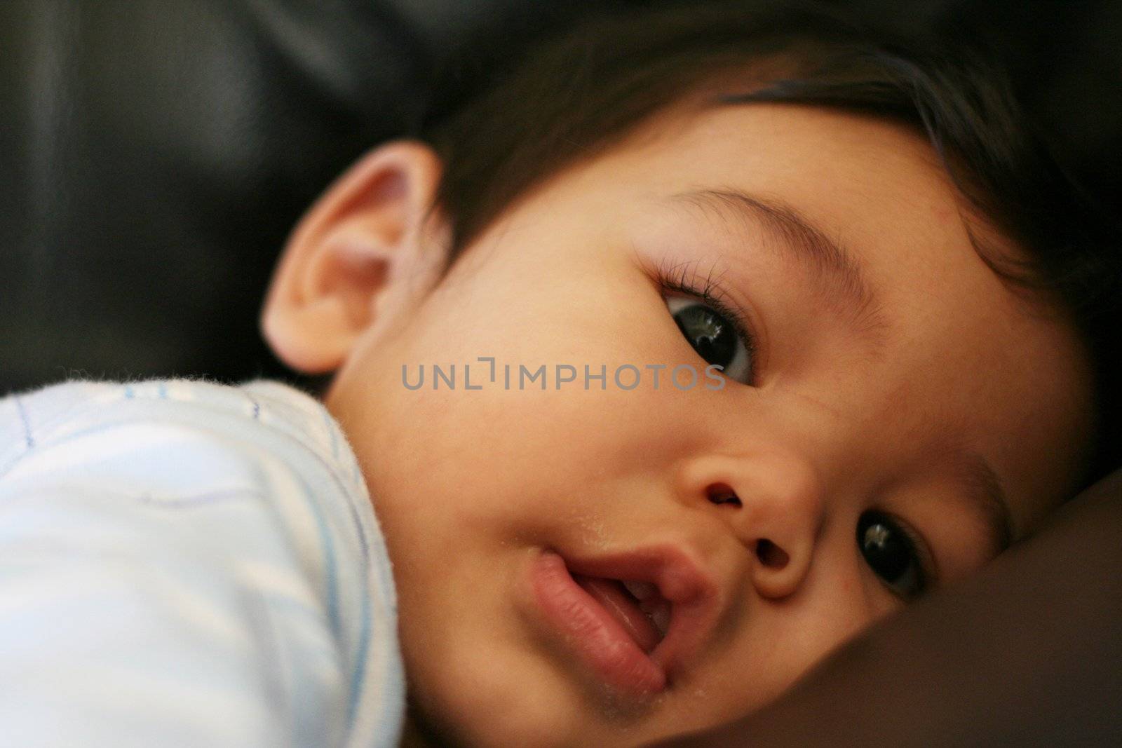 Baby boy quietly lying on couchBaby boy happily sucking fist on couch