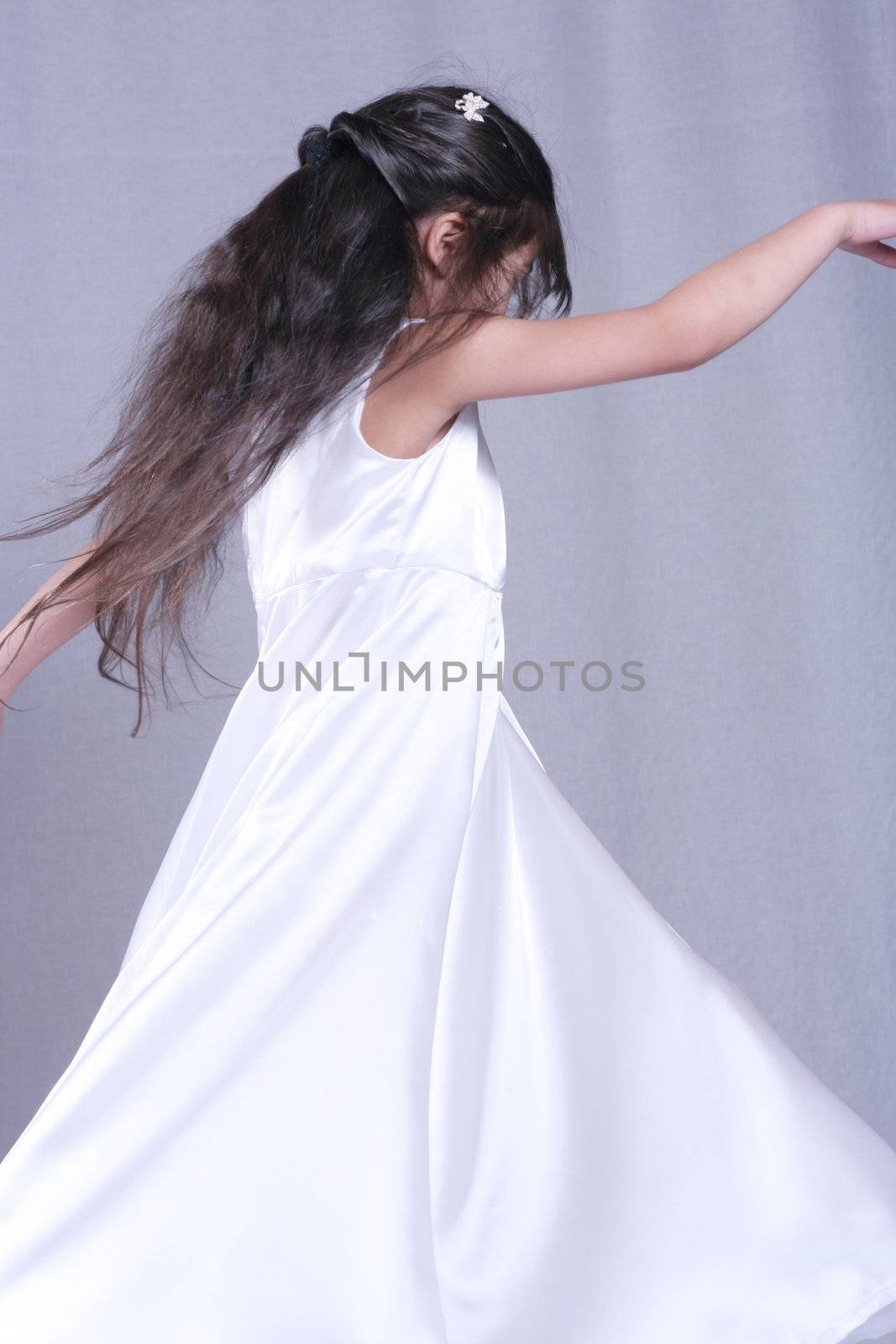 Beautiful little girl in white satin gown twirling playfully. Part Asian, Scandinavian background.