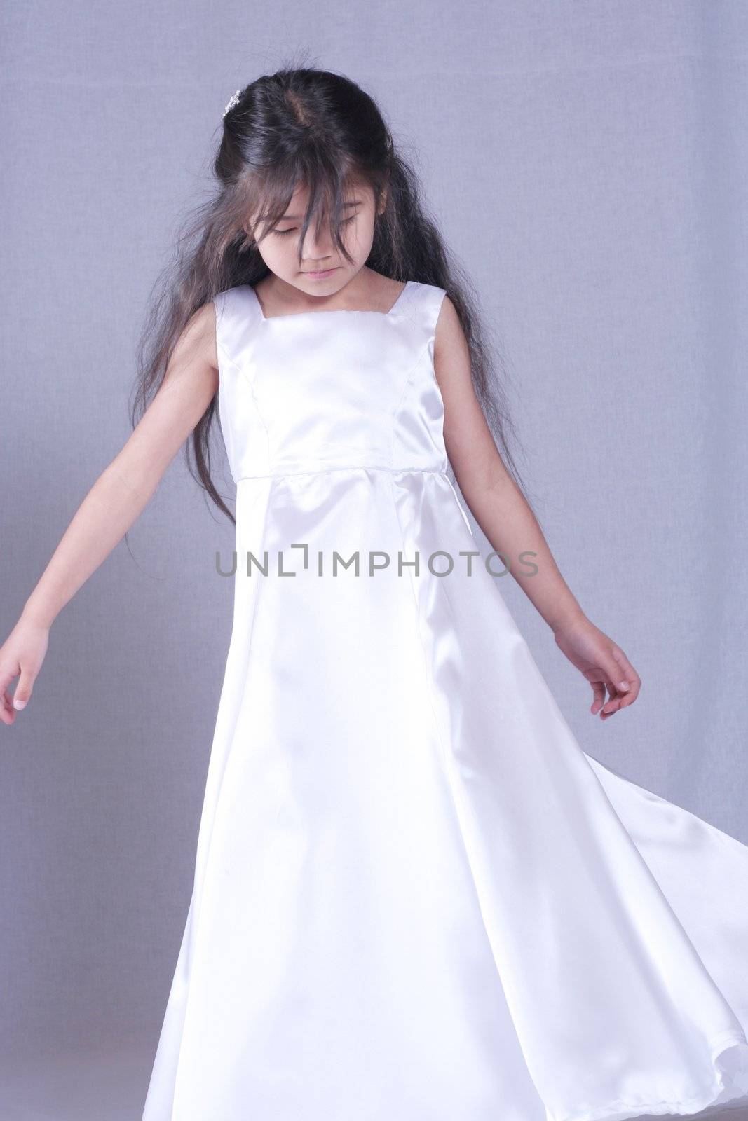 Beautiful little girl in white satin gown twirling playfully. Part Asian, Scandinavian background.