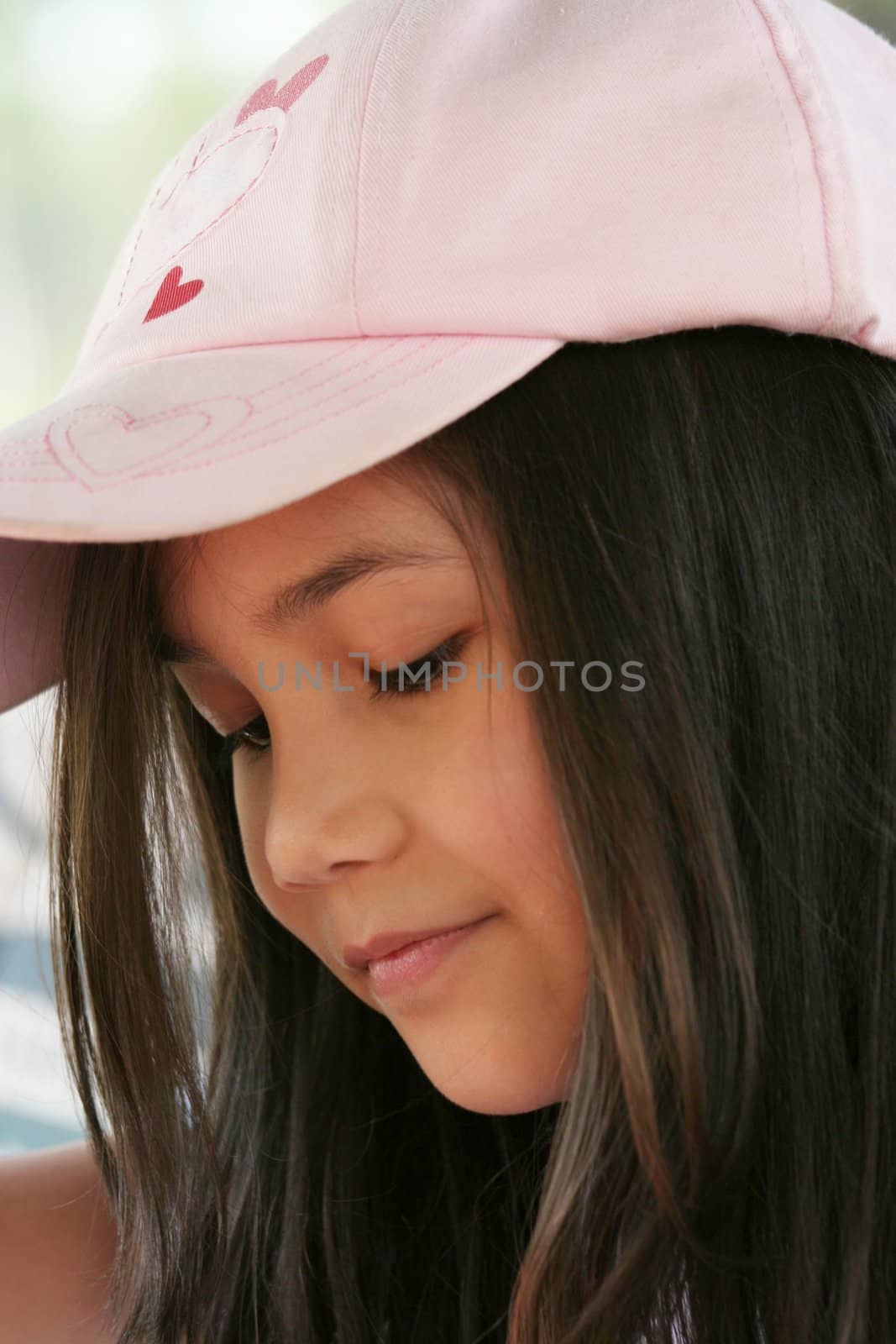 Child in pink cap looking downwards, outdoors in summer. Part asian, scandinavian descent.