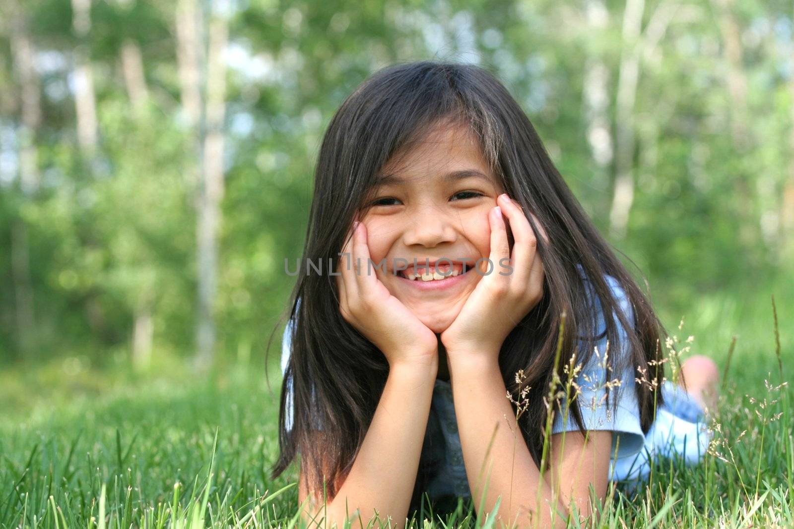 Child lying on grass with a thoughtful expression. Part asian, scandinavian background. by jarenwicklund