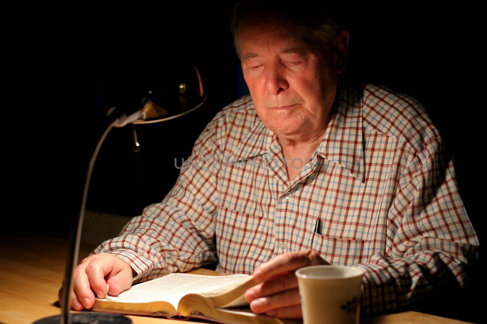 ELderly man reading Bible by lampligh