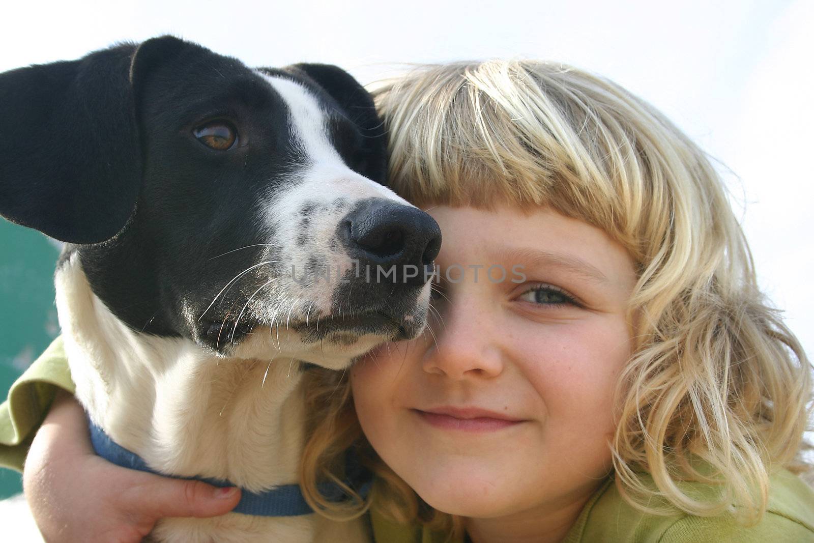 A 6 year old girl is cuddling her dog. Closeup of their faces