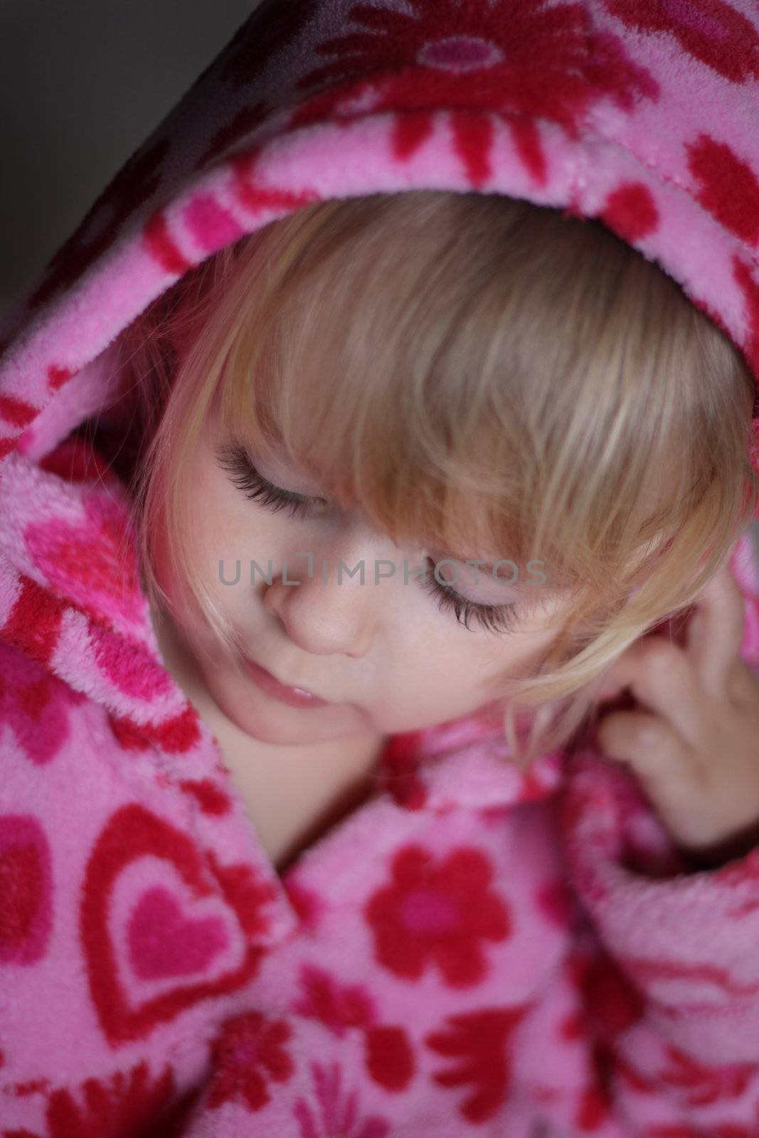 A soft focus close up vertical portrait of a 3 year old girl with eyes closed