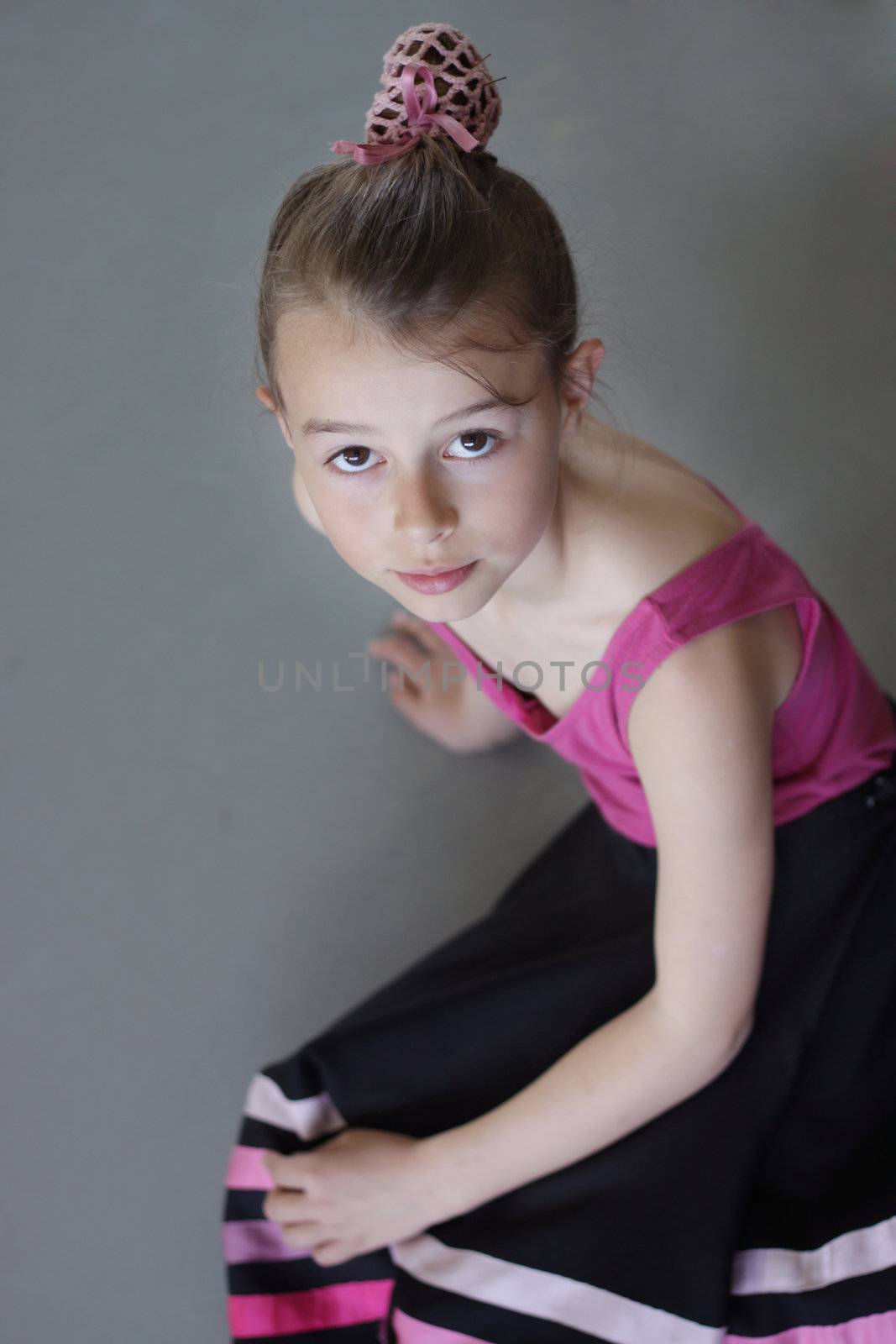 A young girl dressed for ballet sits on the floor and looks up at the camera