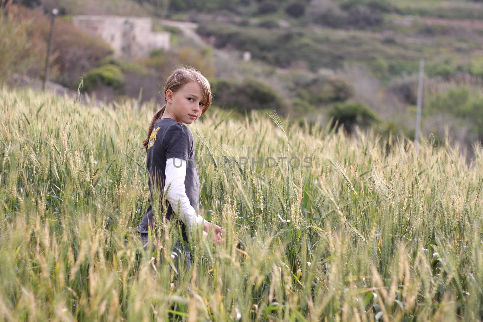 A young girl standing in a field, turning towards the camera. Positive feeling