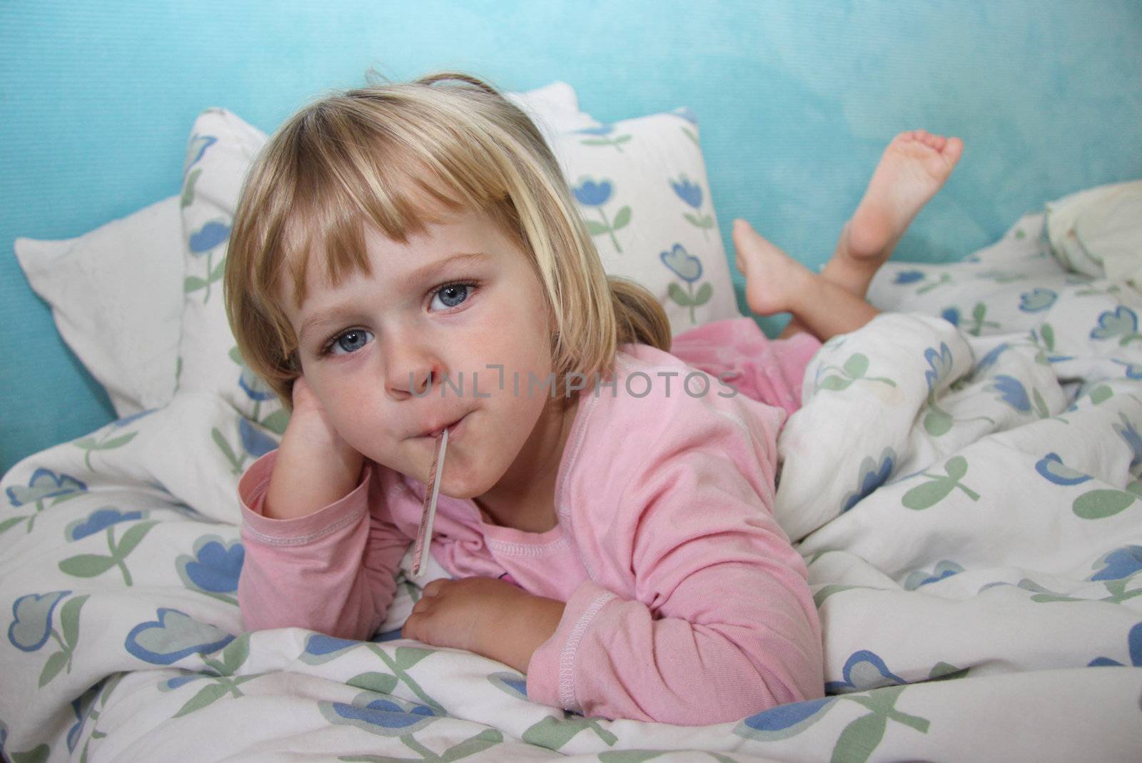 A sick girl lying in bed, having her temperature checked