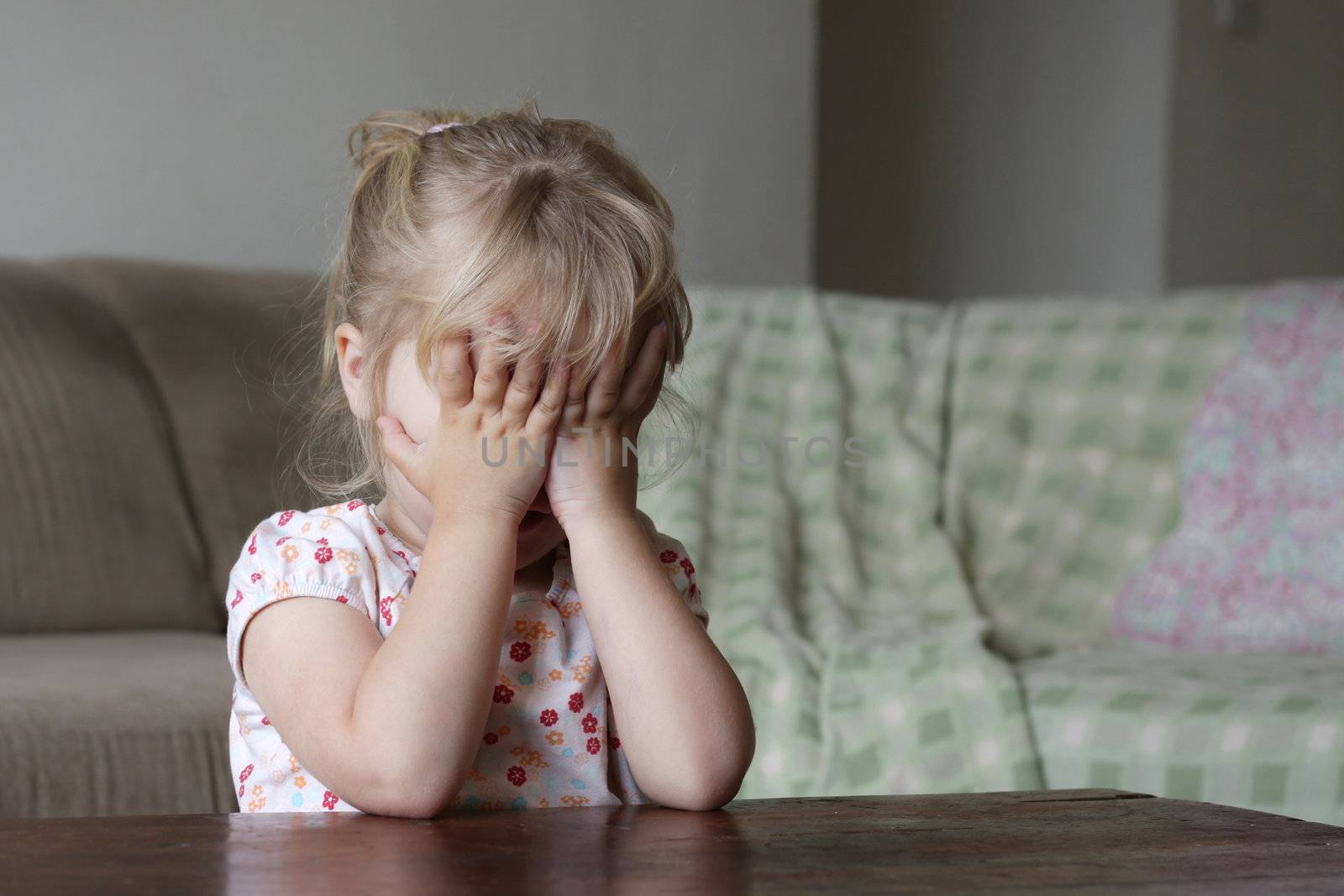 A toddler hiding her face behind her hands, could be scared, playing, counting, shy, or ashamed