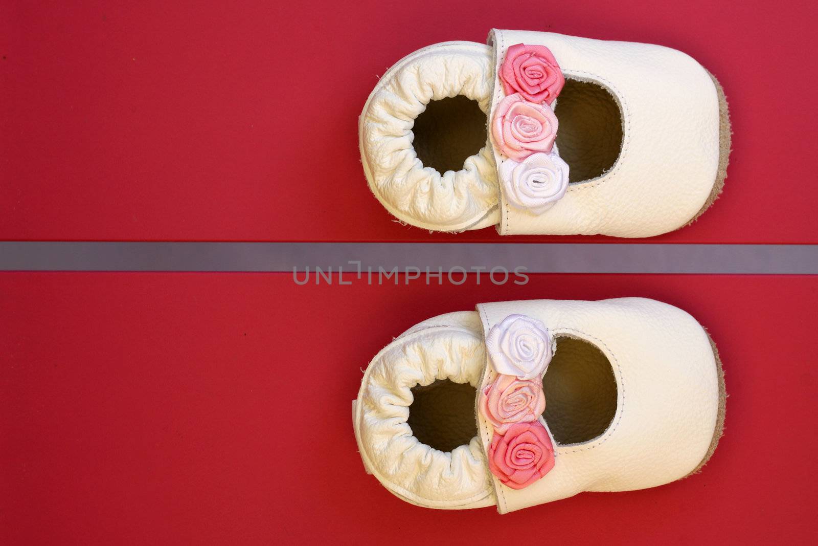 Beautiful tiny cream coloured baby princess shoes with roses, photographed on a red chair