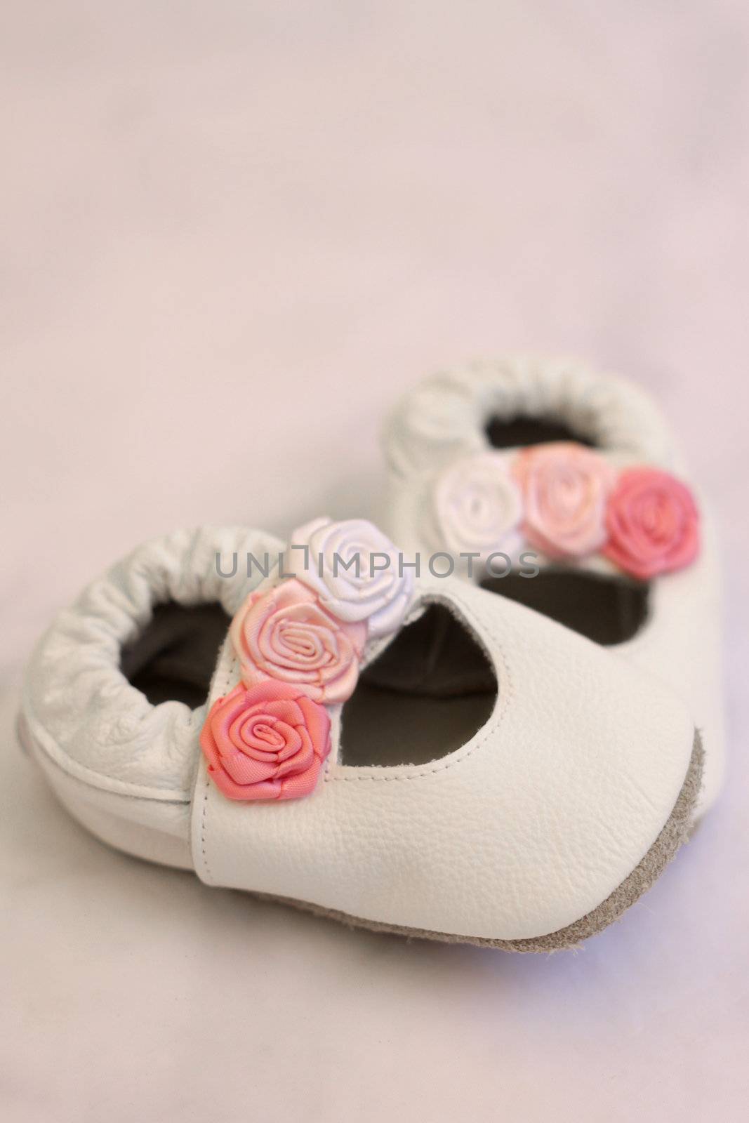 White leather shoes with roses for a small baby girl. Shot on grey background, soft focus