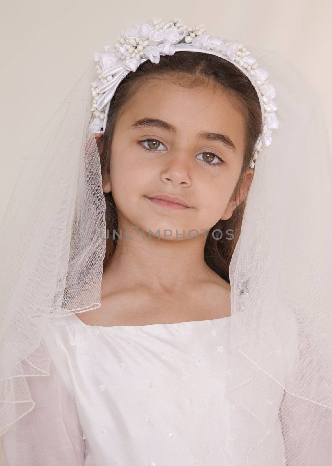 Portrait of a serious looking young girl who is celebrating her holy communion. The girl looks straight into the camera with big beautiful eyes.