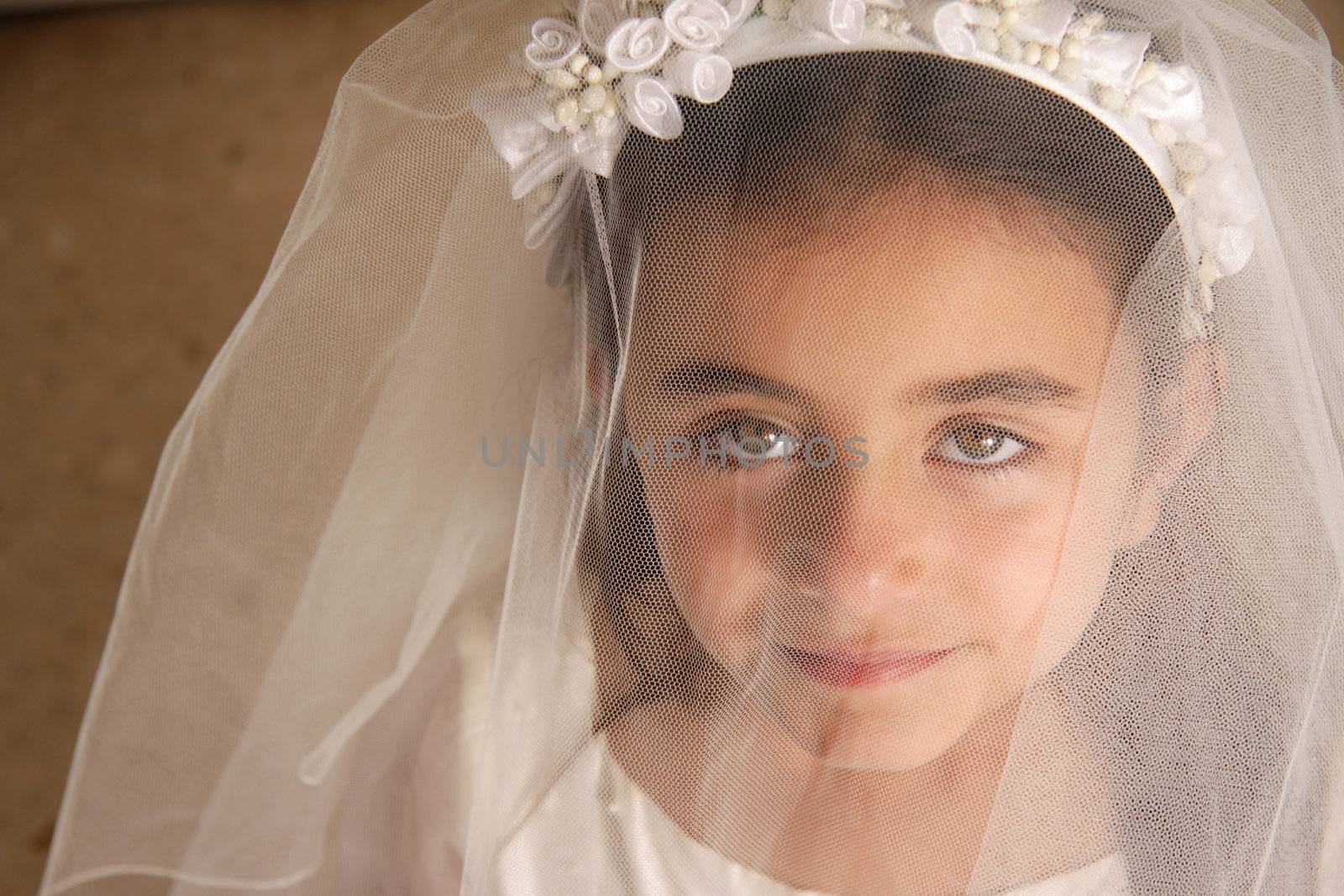 A young girl in her holy communion outfit looking at the camera from behind her veil. Stunning green eyes