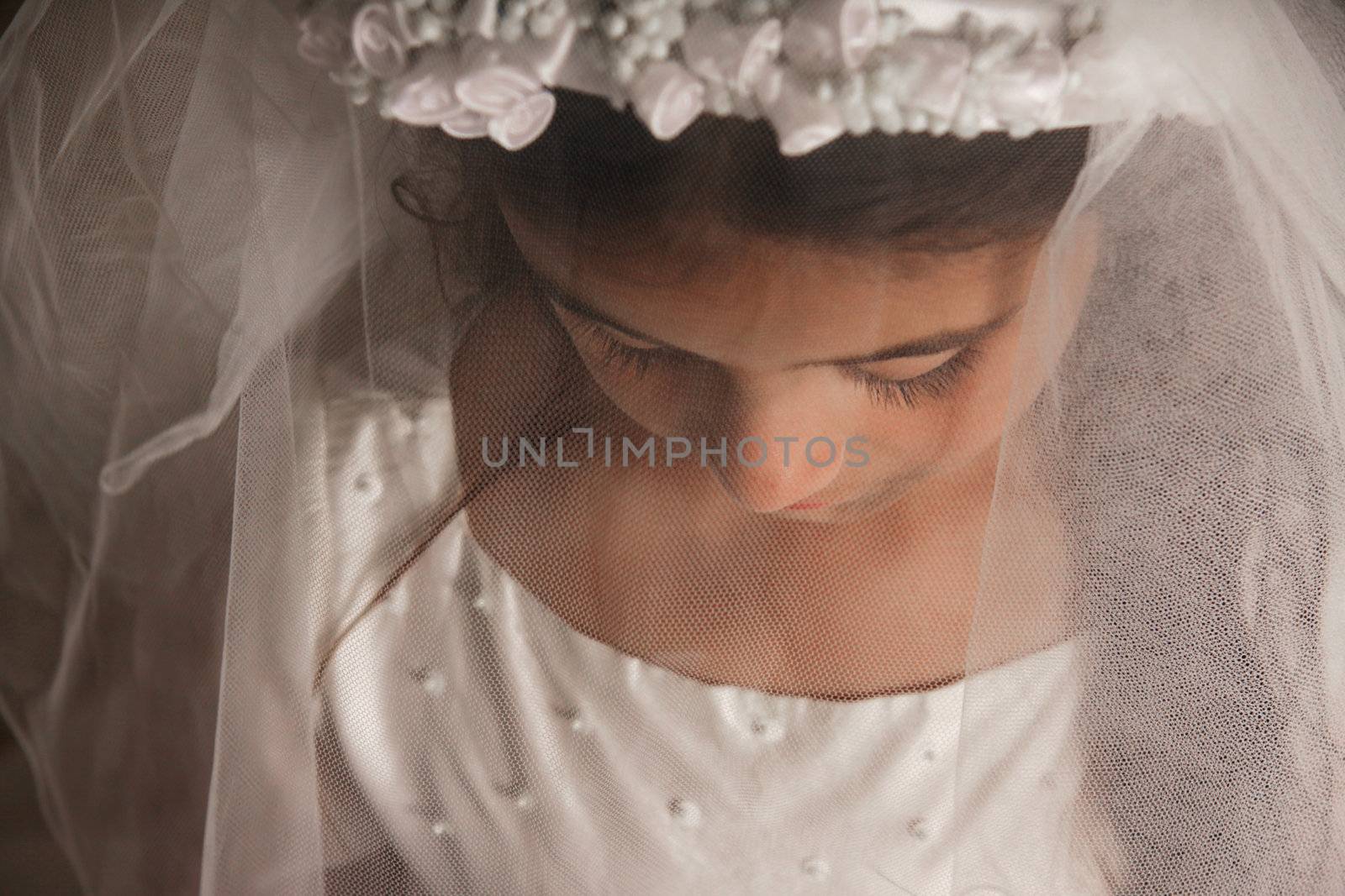 Girl celebrating her First Communion. Her face is covered by her veil, and she is looking down. Sad, serious feeling. Horizontal photo