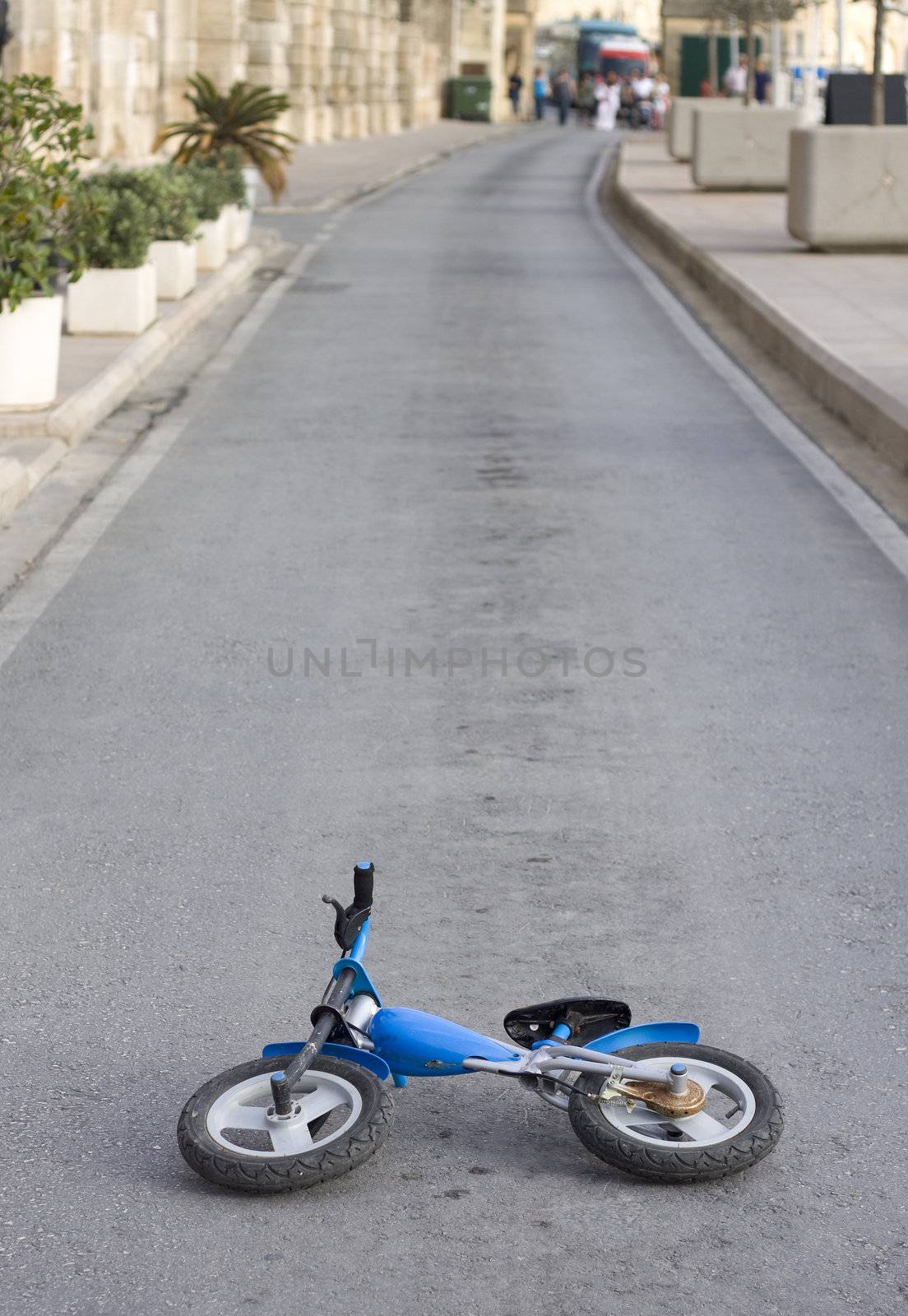An old kids push bike is abandoned in the middle of the road. A crowd looking at the far distance
