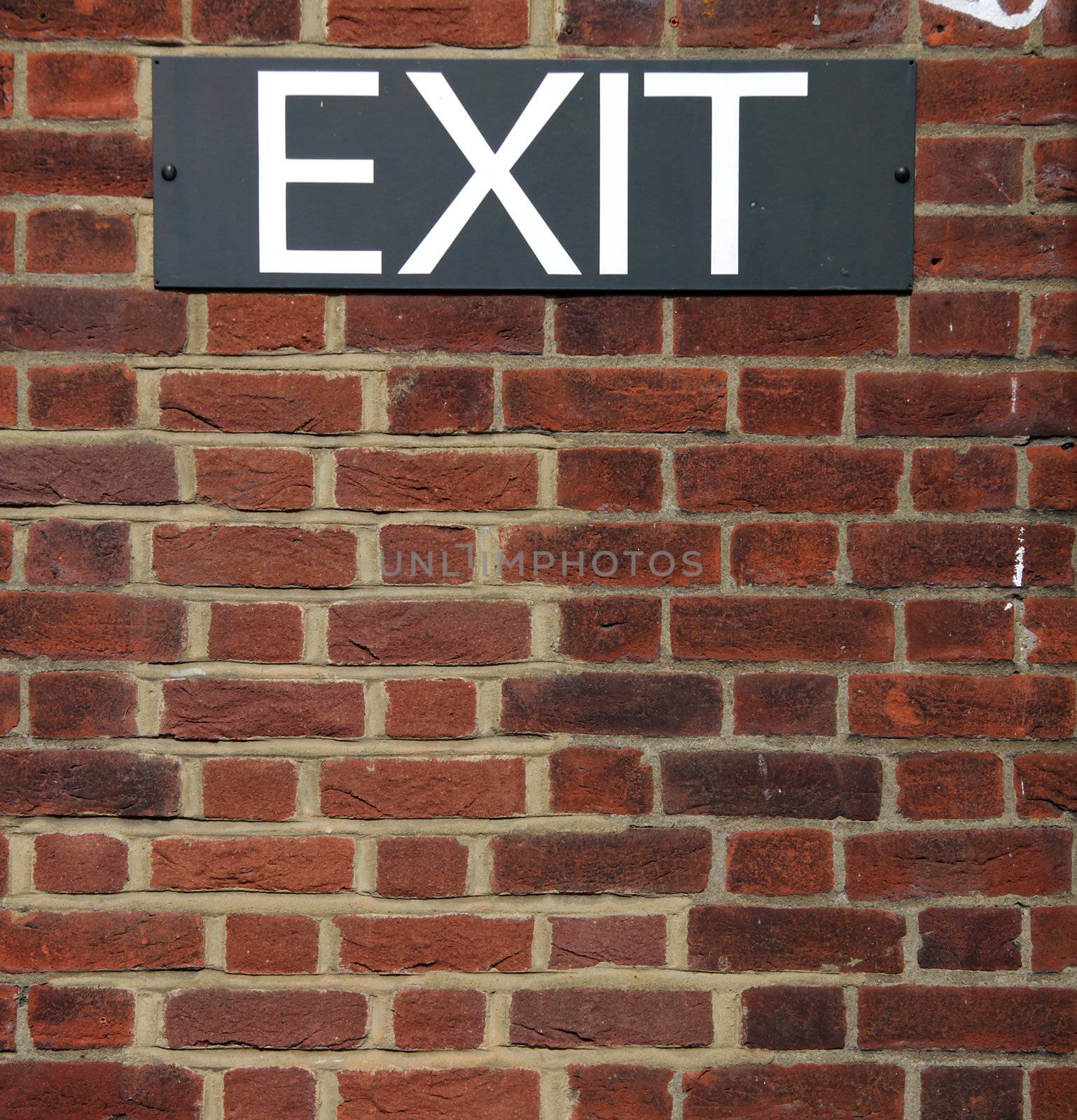 A black and white exit sign put up on a red brick wall