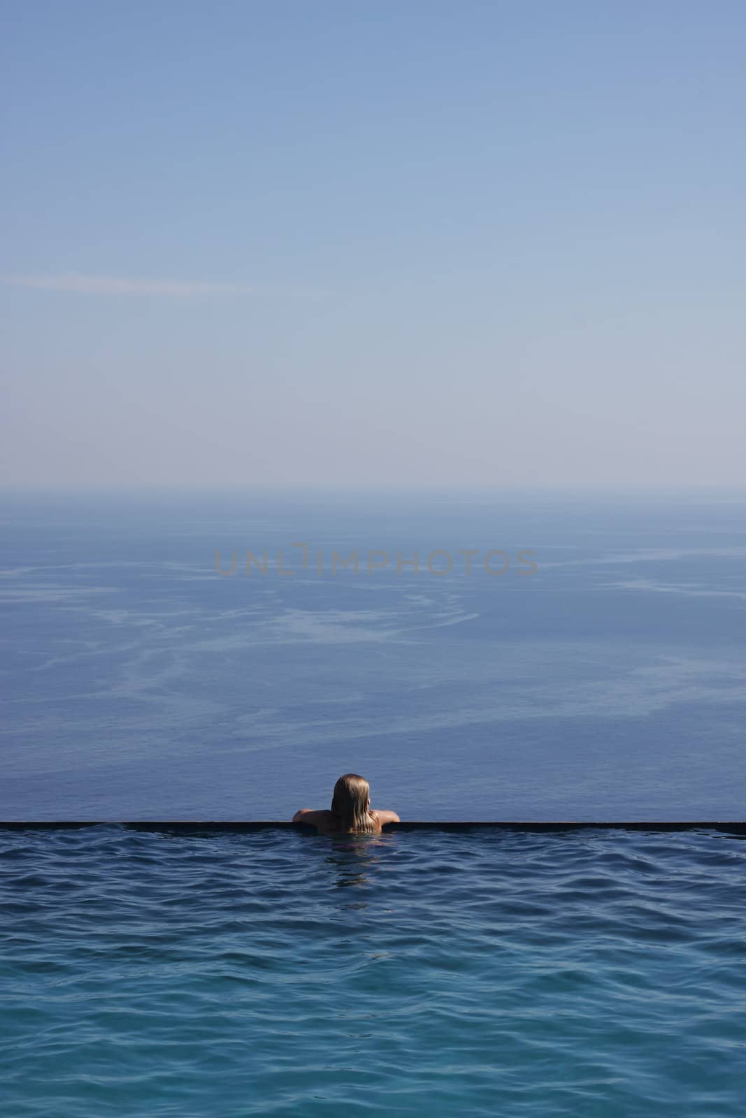 Girl looking at the endless sea view from an infinity pool