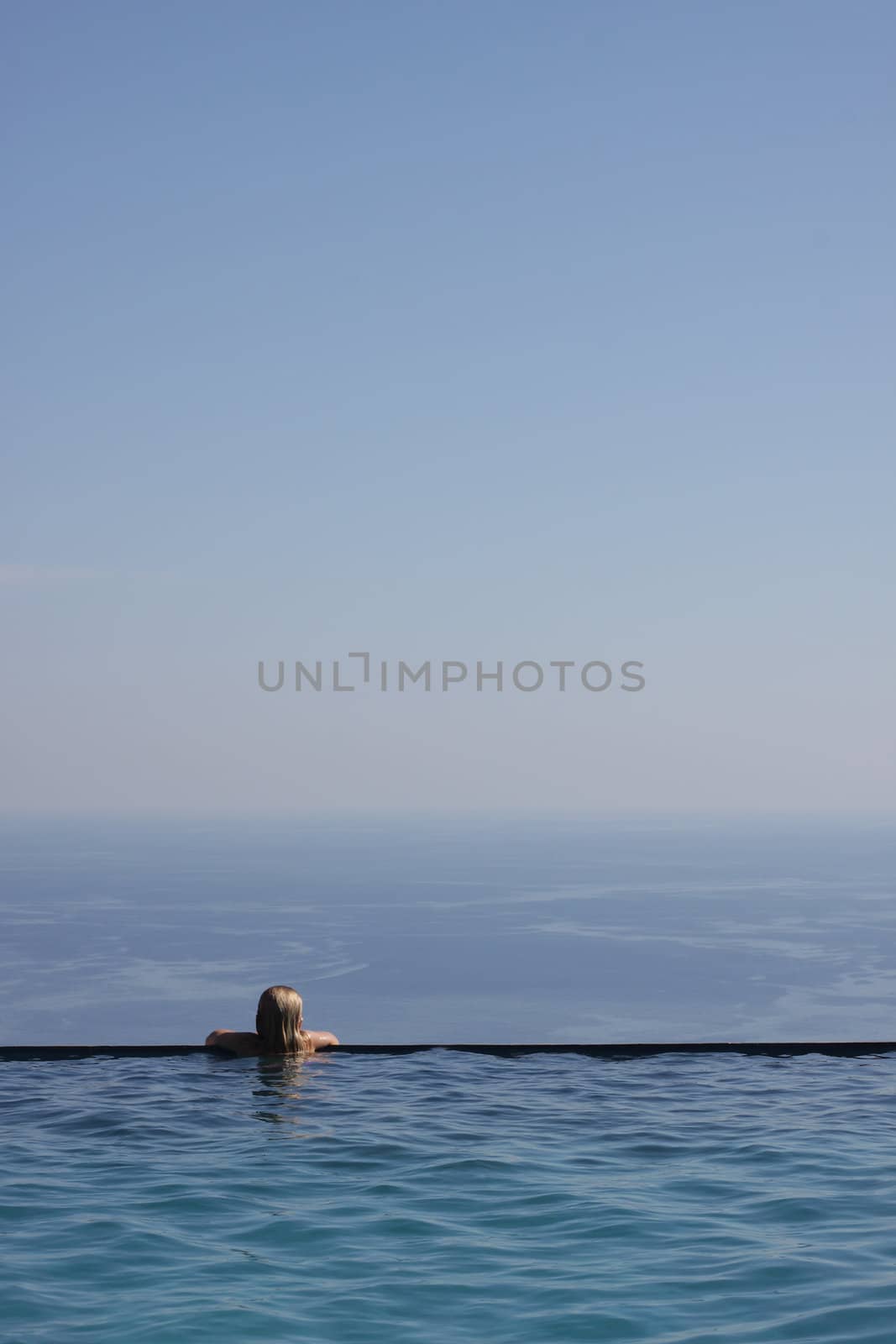 Girl relaxing at the end of an infinity pool, looking at an amazing view of the Mediterranean Sea. Copy space to the right and above