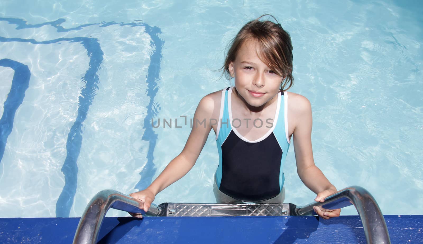 A ten year old blonde girl standing on the ladder to a swimmingpool