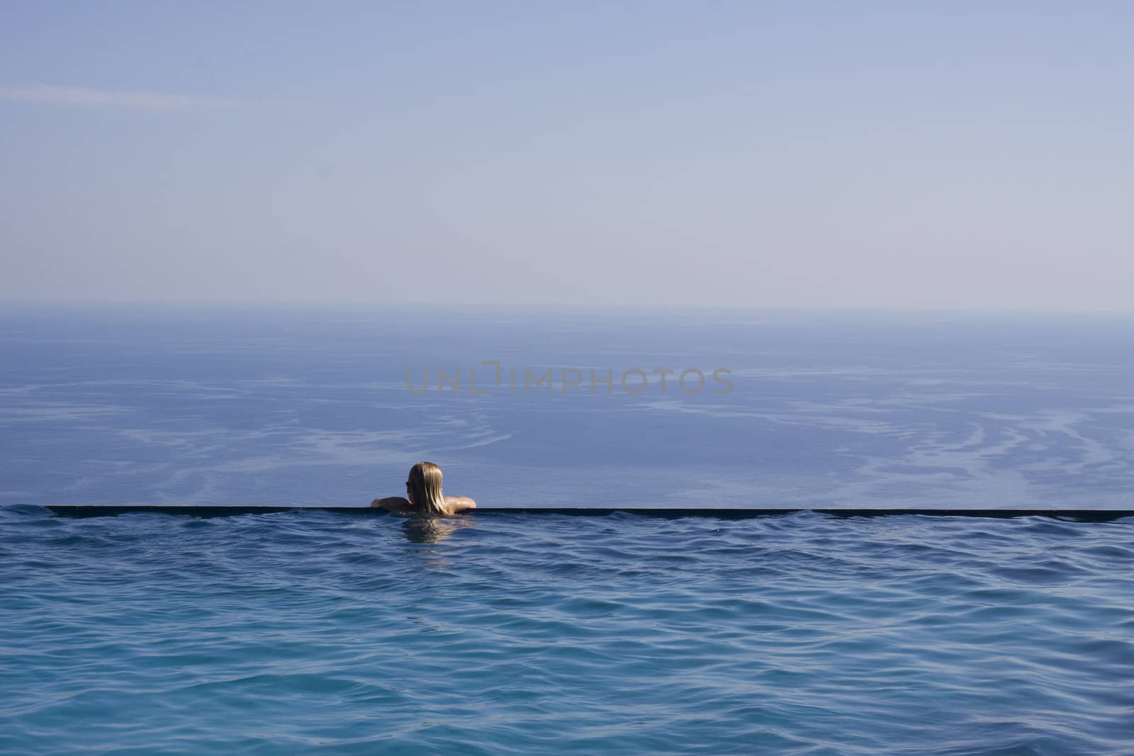 A girl resting at the end of a stunning infinity pool. Space for text